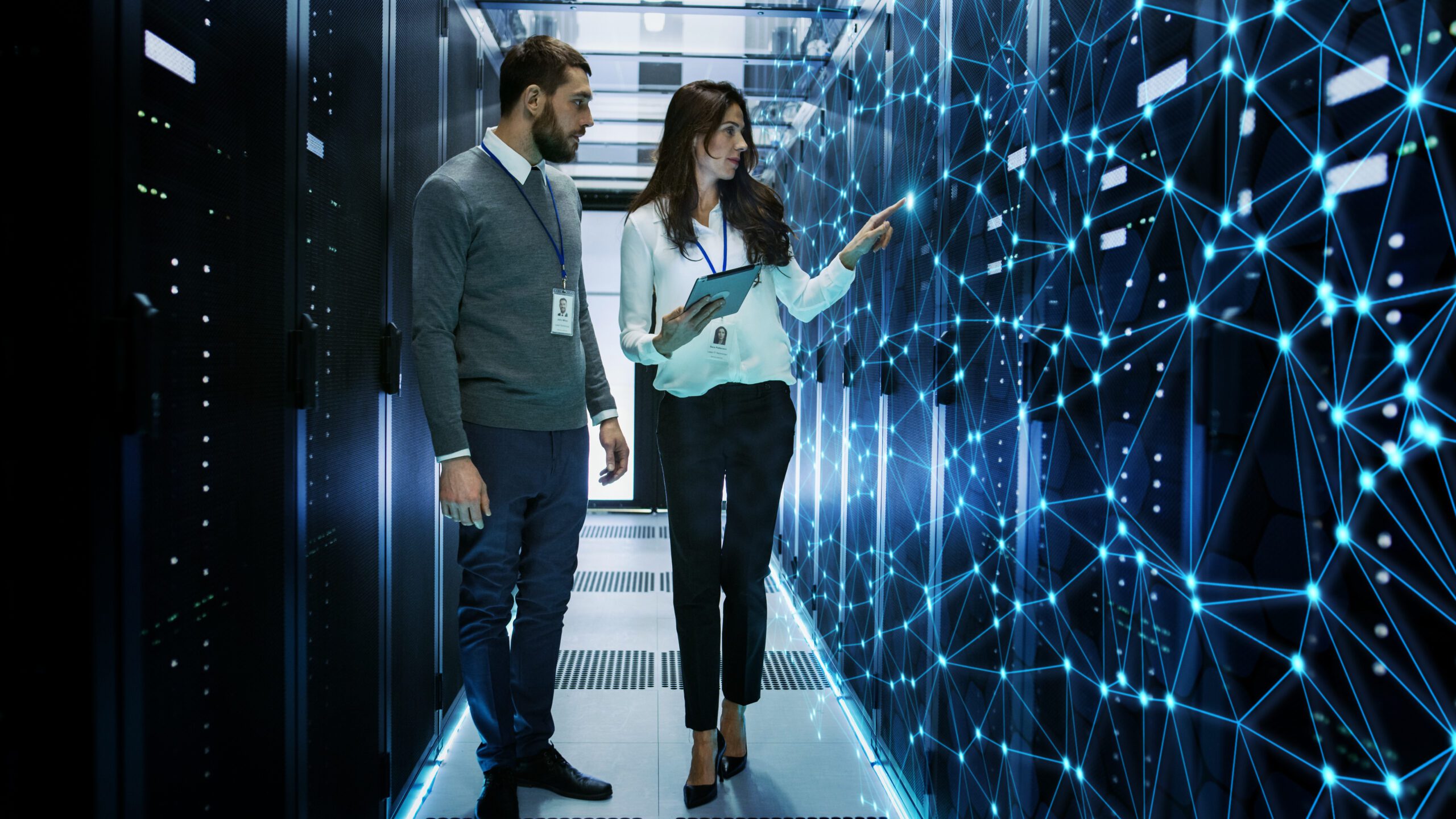 Female and Male IT Engineers Discussing Technical Details in a Working Data Center/ Server Room with Internet Connection Visualization